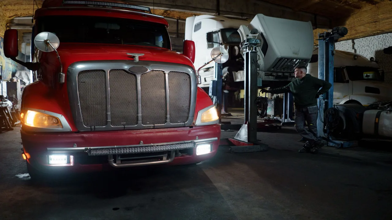 Red truck in a garage with mechanic and elevated vehicles undergoing maintenance
